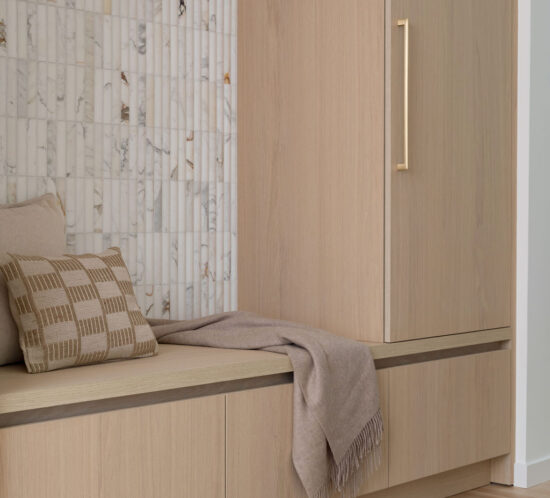 Entry bench with light oak cabinetry, shadow reveal detail, integrated storage, and vertical stone tile wall.