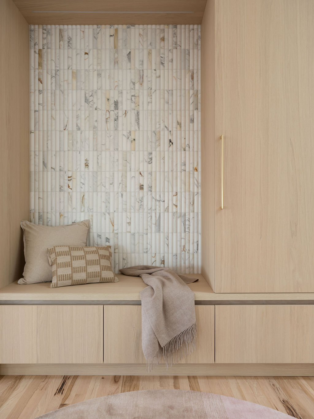 Entry bench with light oak cabinetry, integrated lighting, shadow reveal, and vertical stone tile backdrop.