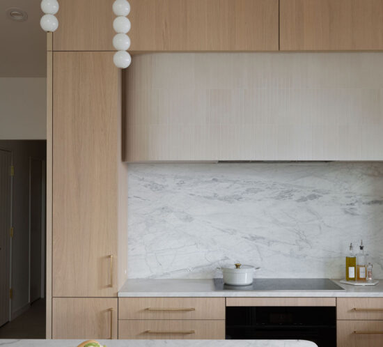 Milk oak kitchen cabinetry with marble backsplash and integrated upper storage wall.