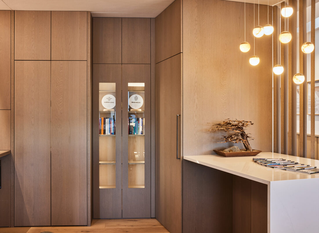 Manhattan oak showroom cabinetry with pivot pocket door and Boyd Callisto pendant lighting